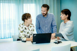 Tre personer som samtalar och tittar på en dator skärm på ett ljusblått kontor